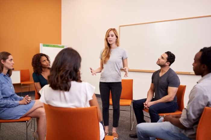 woman-standing-to-address-group-of-men-and-women-a-2024-10-22-13-26-09-utc